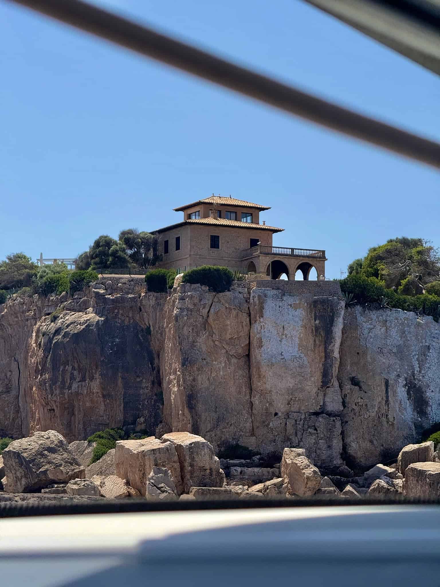 Rugged cliffside villa with Mediterranean architecture, surrounded by greenery, under a clear blue sky. A scenic coastal house offering ocean views and outdoor terraces, representing luxury seaside living.