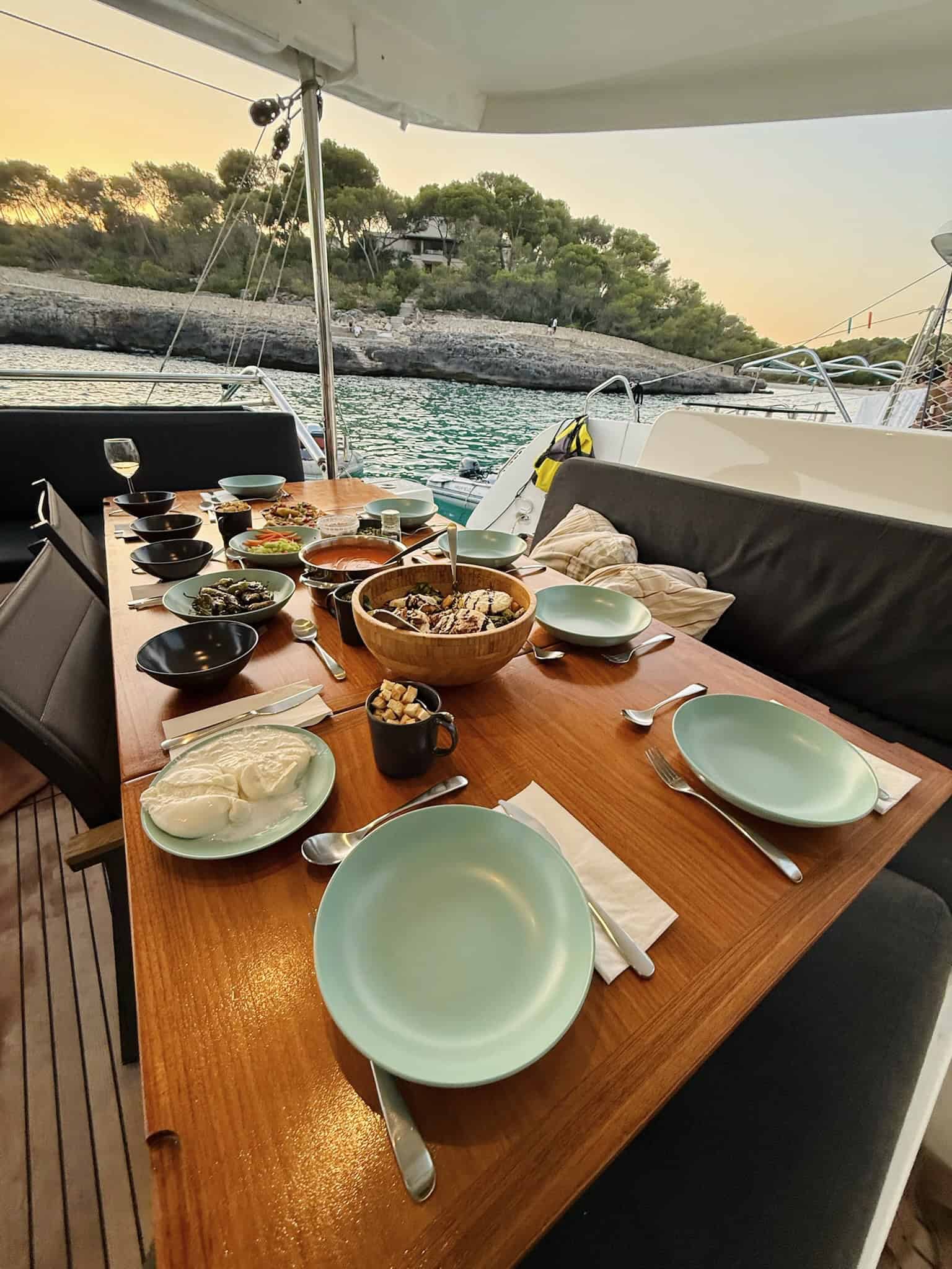 Luxurious yacht dining table set with a variety of dishes, overlooking a serene water landscape at sunset, showcasing outdoor marine leisure and gourmet dining experiences.