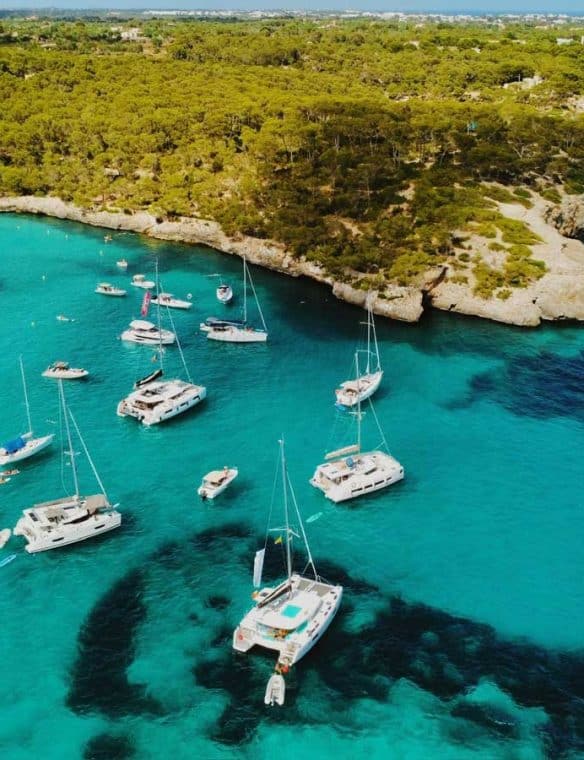Boats anchored in a picturesque turquoise bay surrounded by lush greenery and rocky cliffs, perfect for luxury sailing holidays and Mediterranean seaside adventures.