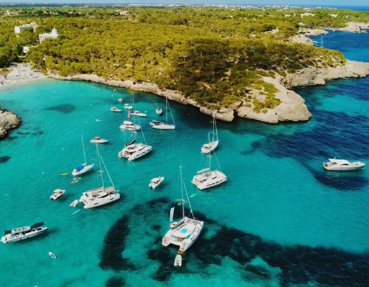 Boats anchored in a picturesque turquoise bay surrounded by lush greenery and rocky cliffs, perfect for luxury sailing holidays and Mediterranean seaside adventures.