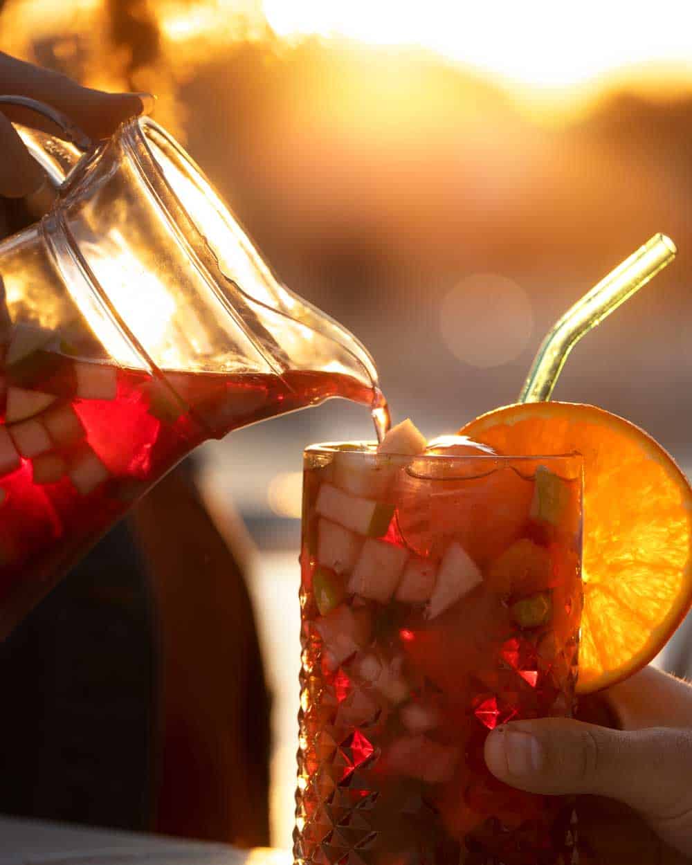 Refreshing fruit punch with diced fruit, served in a textured glass with an orange slice garnish during sunset.