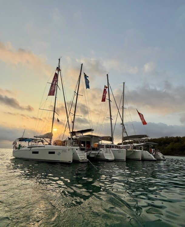 Colourful sailing yachts anchored at sunset on a calm sea, with flags flying, perfect for luxury maritime travel and boat rental services.
