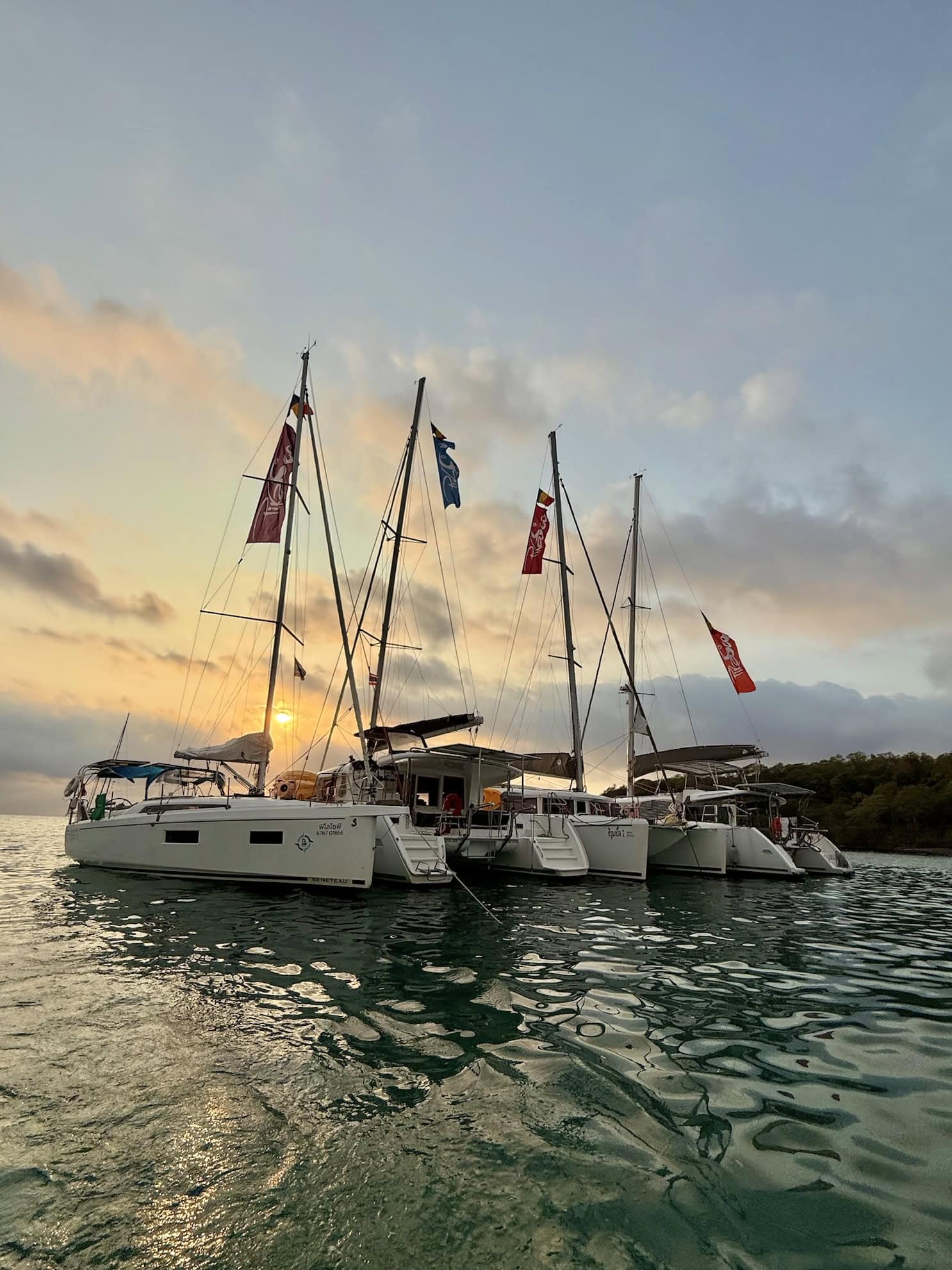 Colourful sailing yachts anchored at sunset on a calm sea, with flags flying, perfect for luxury maritime travel and boat rental services.