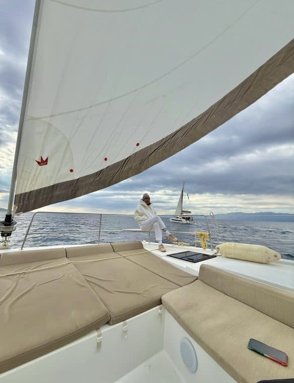 Sailing yacht with comfortable sunbathing area, woman relaxing on deck, expansive ocean views, cloudy sky, modern boat design, leisure, luxury sailing, scenic marine landscape, white yacht interior.