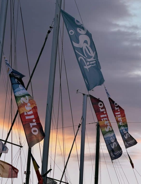 Banners on sailboats with sunset sky in the background, showcasing SeSea Sail flags and promotional material at a marina, emphasizing sailing and maritime activities.