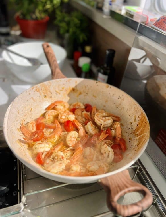 Shrimp and cherry tomatoes cooking in a skillet on a stove. Fresh seafood, nutritious meal, home cooking, seafood dish, healthy meal.