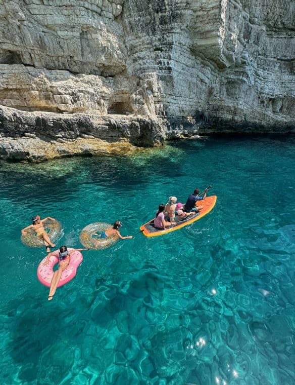 Floating on turquoise waters with inflatable rings and paddleboarding in a stunning rocky cove, enjoying a fun summer day at Pikasea. Perfect location for water activities and scenic natural beauty.