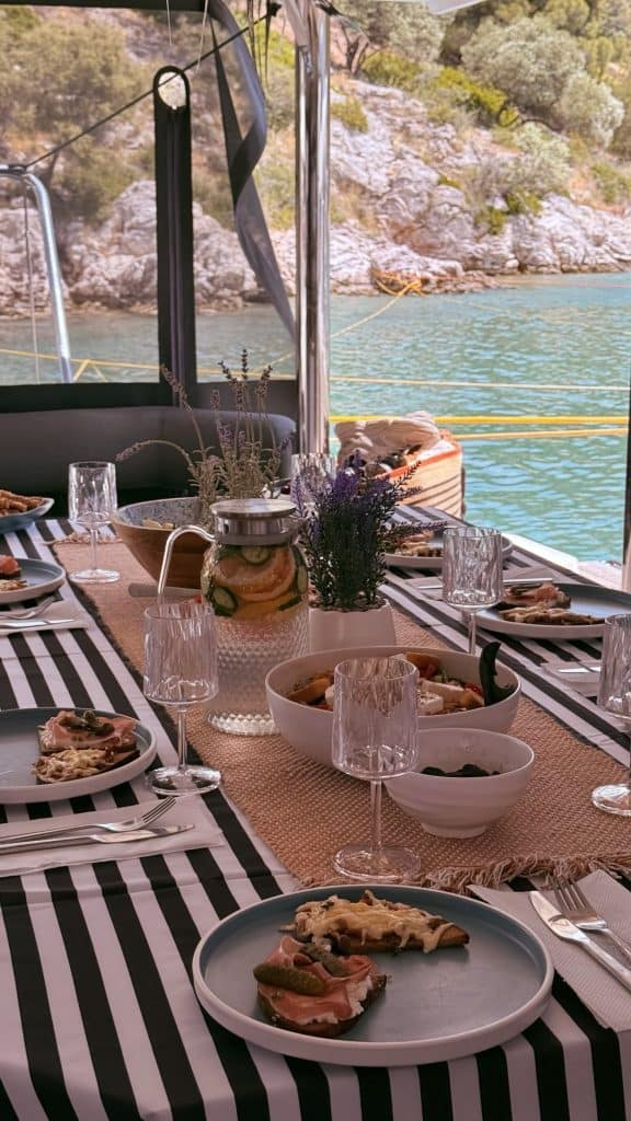 Lavish seaside dining table with Mediterranean dishes and fresh flowers, overlooking turquoise water and rocky coastline, perfect for outdoor oceanfront meals.