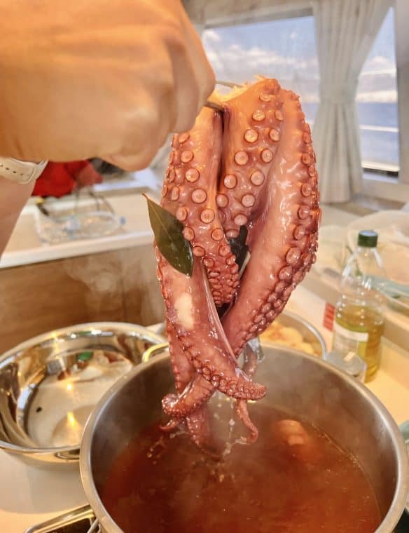 Octopus being cooked in a pot, ready for preparation with herbs and spices, showcasing seafood cuisine for a Mediterranean or seafood restaurant.
