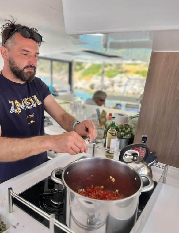 Grilling chef preparing a delicious tomato and garlic sauce in a modern, bright kitchen with scenic outdoor views, highlighting culinary skills and contemporary cooking environment.