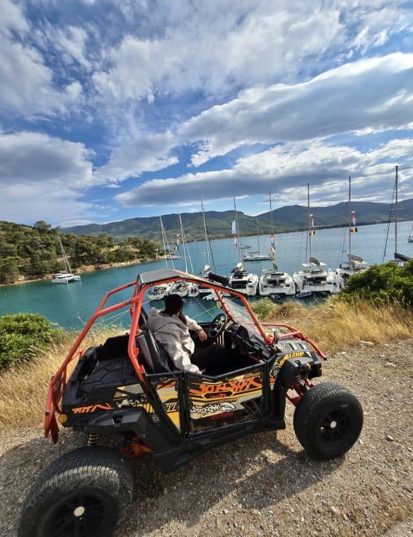 Off-road buggy parked by a marina with sailboats, scenic mountains, and a blue sky with clouds, offering adventurous outdoor experiences near Pikasea.
