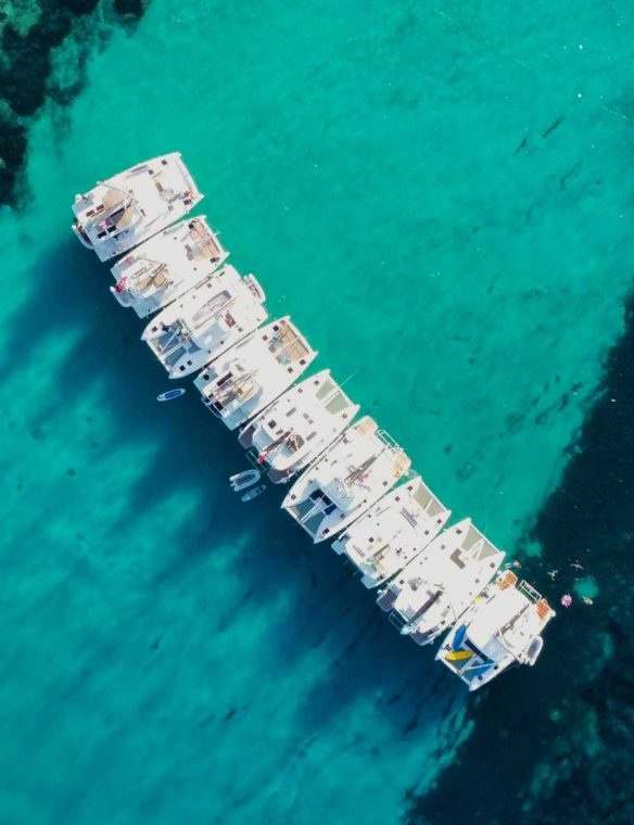 Boats anchored in clear turquoise sea with coral reef, aerial view, tranquil ocean, vacation, summer, travel, marine life, scenic seaside.