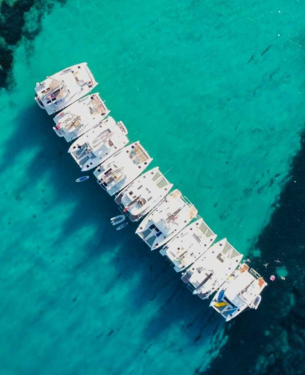 Boats anchored in clear turquoise sea with coral reef, aerial view, tranquil ocean, vacation, summer, travel, marine life, scenic seaside.