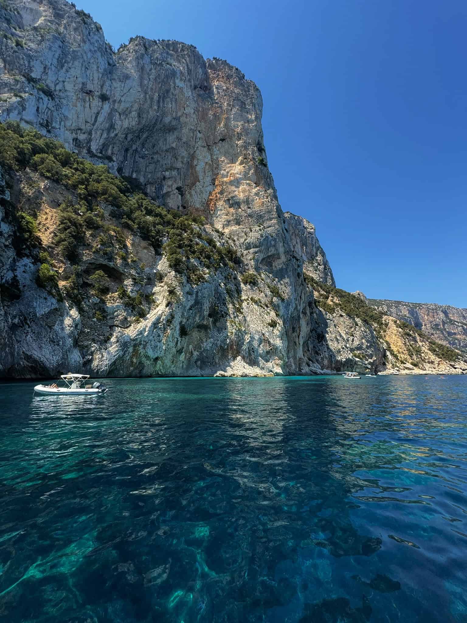 Steep rocky cliffs along the coast with turquoise waters and a small boat, highlighting scenic Mediterranean seaside landscapes and boating activities.