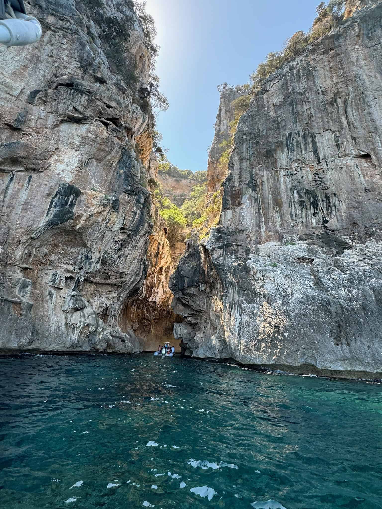 Cliffs and turquoise waters of a scenic sea cave, with a small boat and visitors exploring the natural rock formations and adventurous landscape at Pikasea.