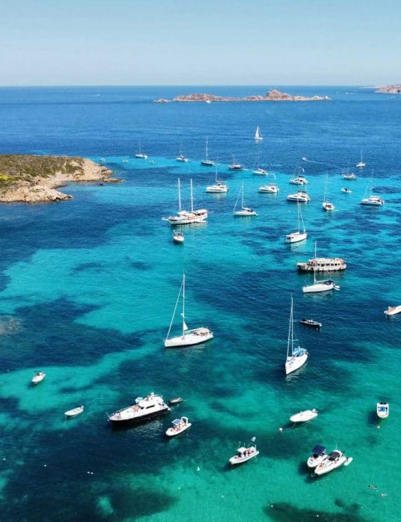 Sailboats anchored in calm azure sea with islands in the background, overlooking a beautiful coastal landscape on a sunny day.