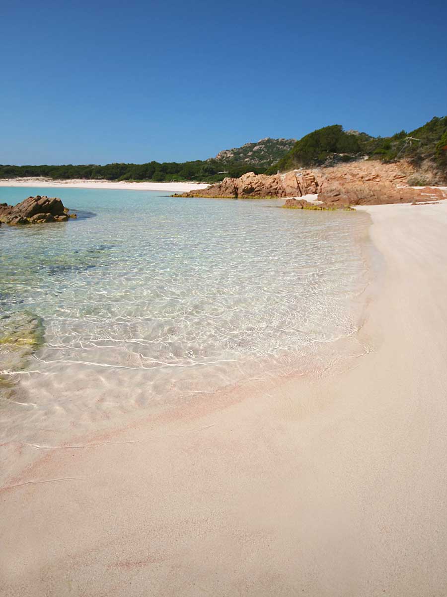 Tranquil beach with clear turquoise water, white sand, rocky outcrops, lush green cliffs, and a bright blue sky, ideal for relaxing holidays and seaside adventures.