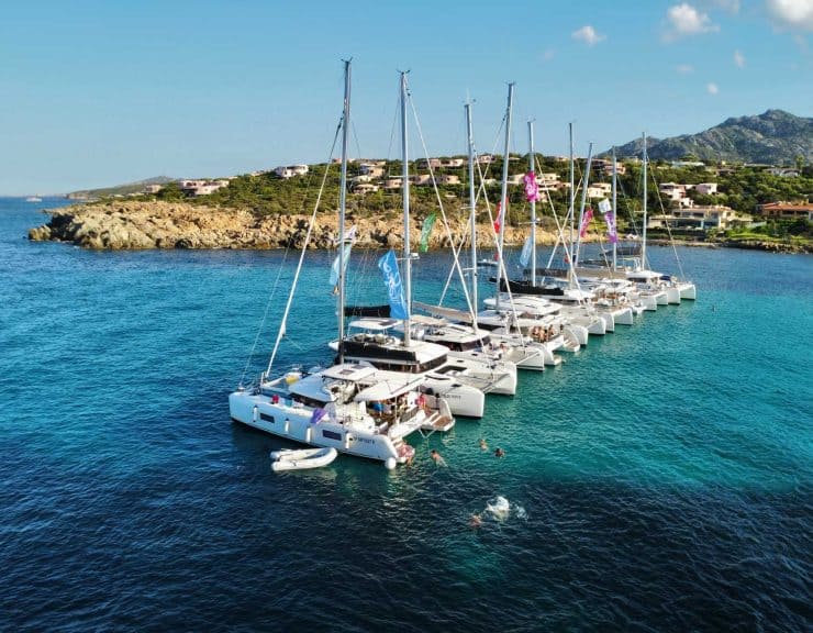 Luxury sailboats docked in a scenic bay with clear turquoise water and hillside residential area in the background.