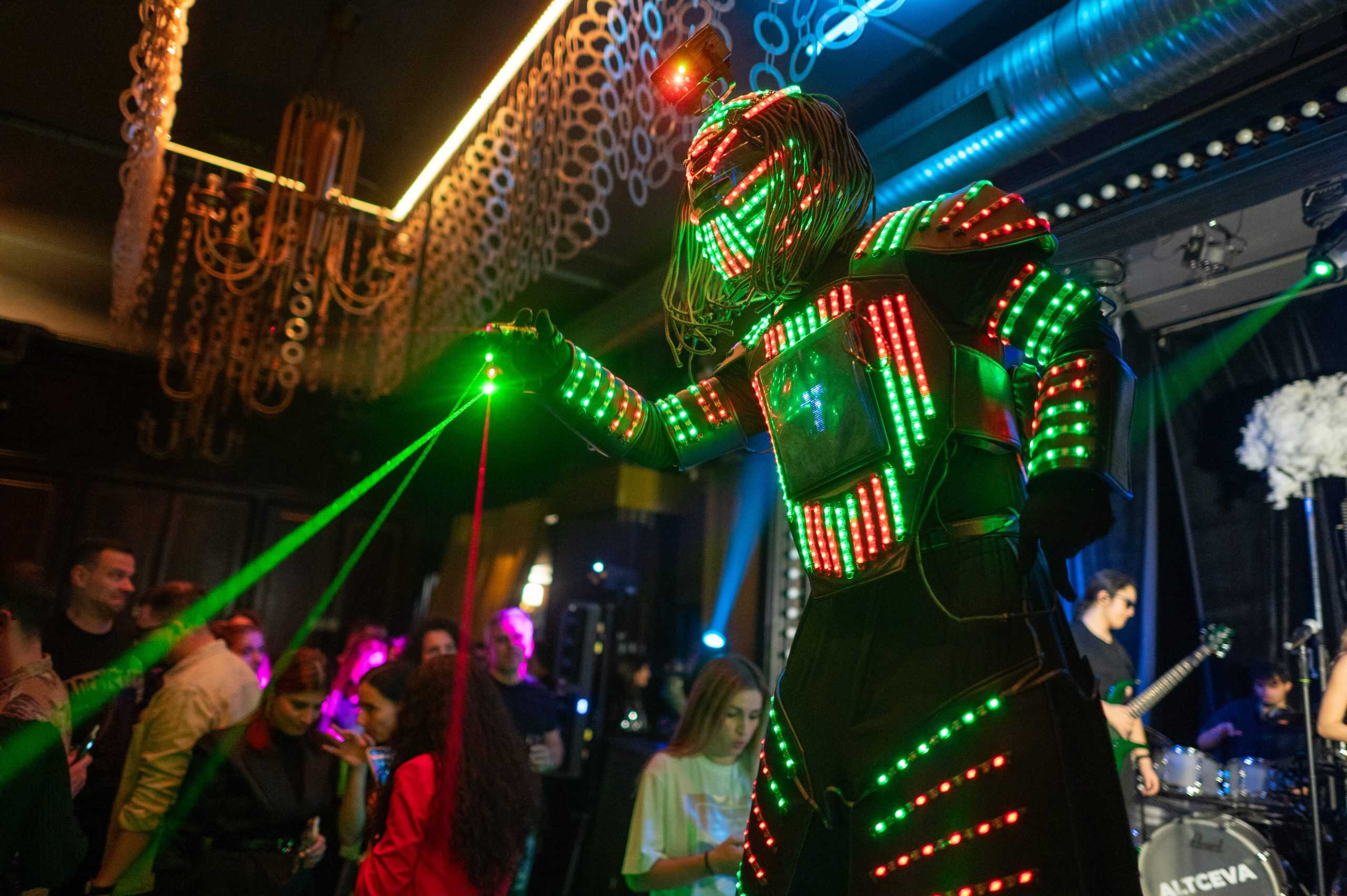Vibrant LED performer wearing an illuminated futuristic costume on stage at a concert, creating a dynamic visual experience with green and red lights in a lively entertainment venue.