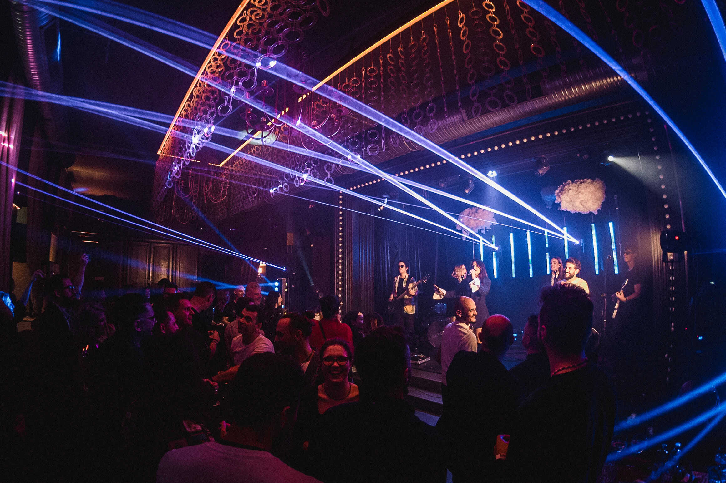 Vibrant live music performance at a club with colourful laser lights, energetic crowd, and dynamic stage lighting creating an exciting nightlife atmosphere.