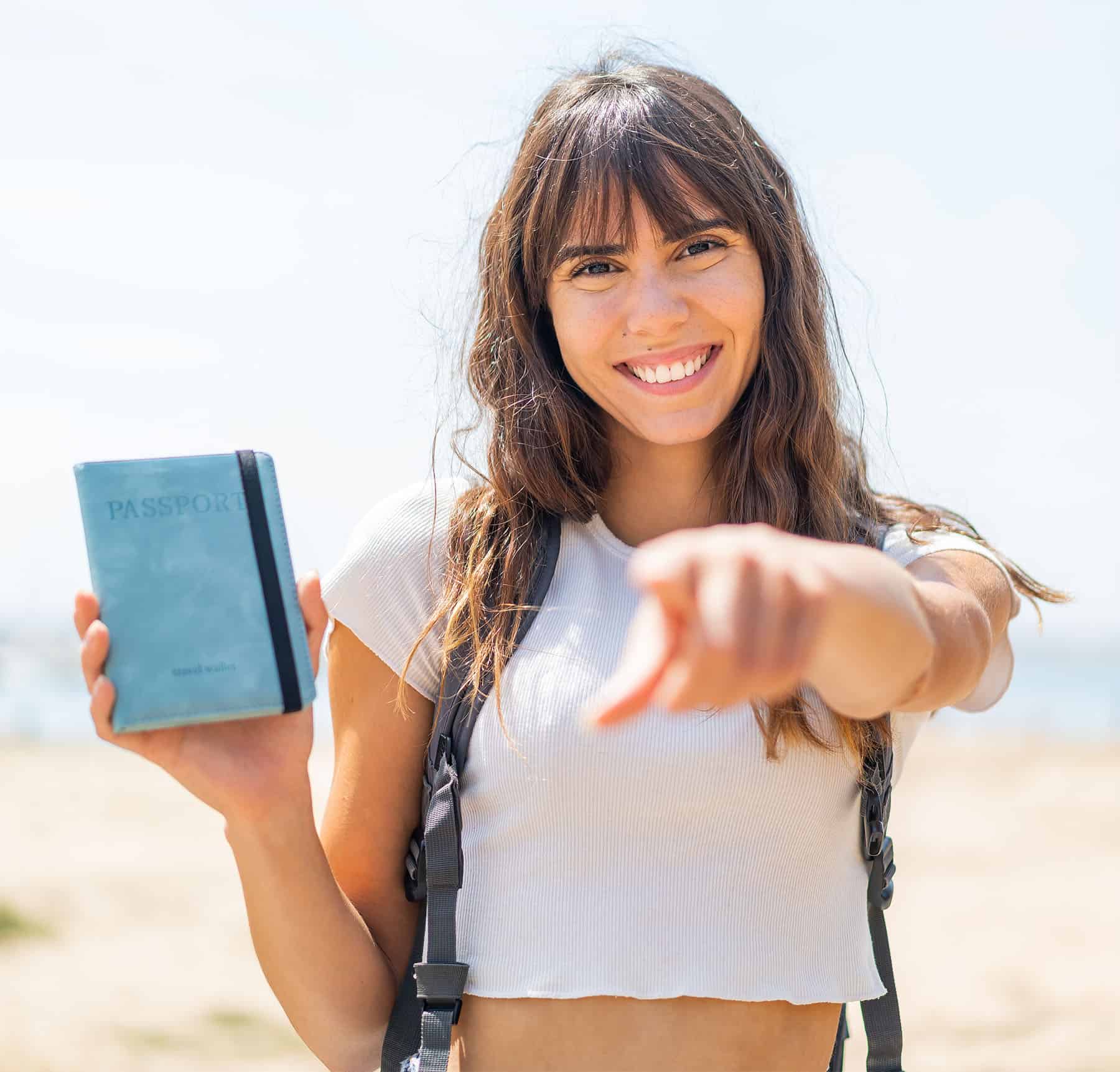 Young woman smiling on the beach holding a passport, promoting travel and festival excitement for Sky & Sea Fest 2026 by Pikasea and TNT.