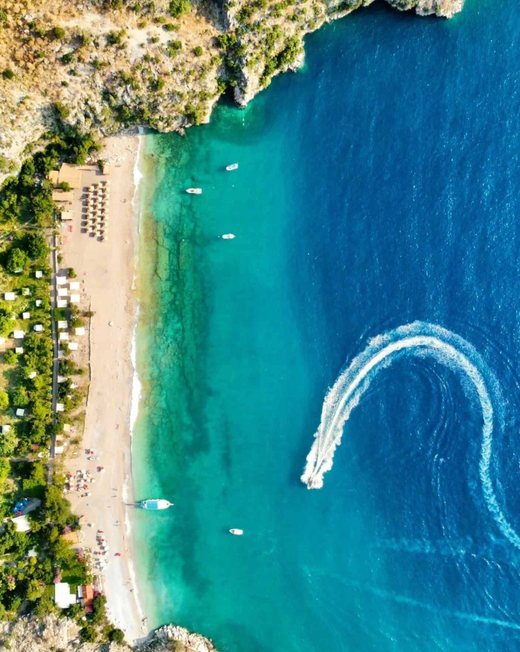 Aerial view of a scenic Tenerife beach featuring turquoise waters, boats, and a sandy shoreline surrounded by lush greenery and rocky cliffs.